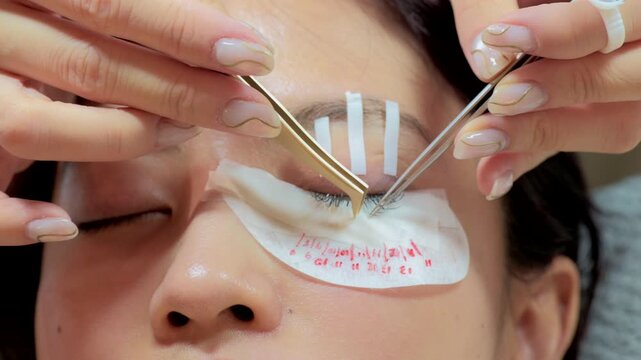 Eyelash extension procedure where cosmetic master expertly uses tweezers to apply fake long lashes on beautiful female, creating glamorous and attractive transformation