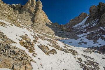View of jagged cliffs and snowy terrain converge under a clear blue sky, creating a stark contrast of textures and colors, Litochoro, Larisa, Greece.