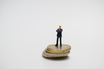 Miniatur-Businessmann steht auf einem Stapel Euromünzen – Symbolbild für Geld und wirtschaftliche Macht