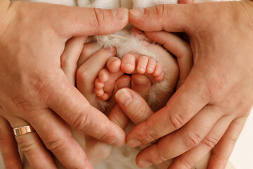 Close-up of newborn baby tiny feet hugged by the older brother and mother hands, with father fingers forming a heart shape on top, symbolizing family love and protection.