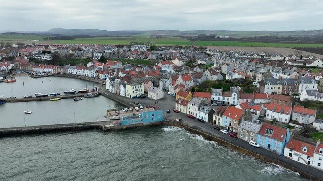 Aerial view of Anstruther harbor with boats, buildings, and water showcasing a quaint coastal scene under a cloudy sky, Anstruther, United Kingdom.