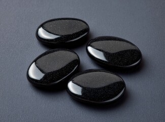 Four smooth, polished, dark black stones arranged on a dark gray surface