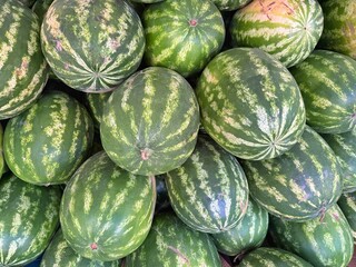 A high-angle shot displays a close arrangement of many ripe, green striped watermelons. Concept of:...
