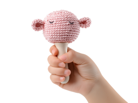 A delicate hand grasps a charming, hand-crocheted baby maraca. The toy, shaped like a friendly creature, adds to the feeling of delight and is an indication of early childhood. 