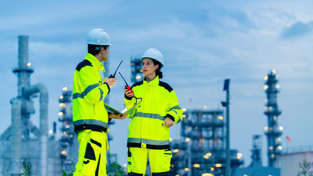 Petrochemical industry engineer teamwork working on laptop computer inspection petroleum oil refinery plant construction site at night. Engineering technician maintaining energy power gas system.