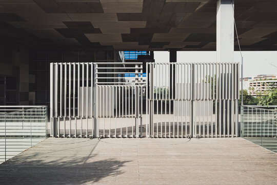 Symmetrical gated passage beneath elevated structure in contemporary city setting, suitable for themes of public space access, geometry, restrictions, and urban regulation or transitions.