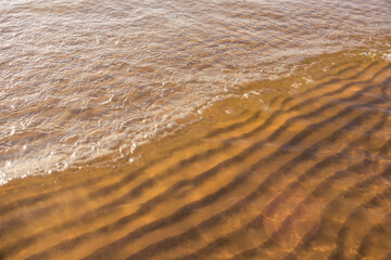 The water is brown and has ripples. The ripples are in the sand and the water is calm