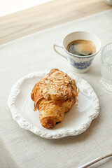 Almond croissant served with black coffee on elegant white plate