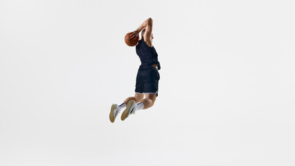 Basketball athlete executing a slam dunk while airborne against a white backdrop. Concept of vertical jump, determination, air control, and basketball training advertisement.