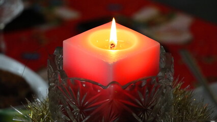 Burning red candle in a glass candlestick on the Christmas table