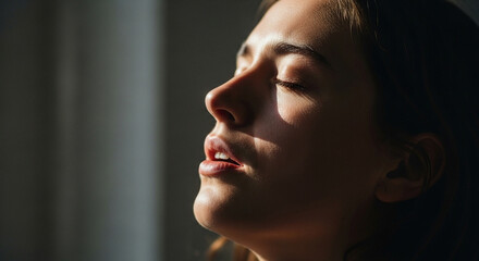 Fototapeta premium Woman's face in sunlight with eyes closed. Peaceful close-up of a woman’s face bathed in sunlight, eyes closed in serenity. 