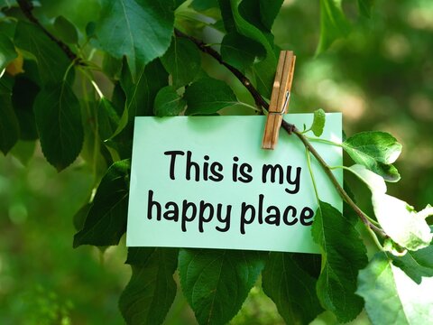 A green paper note with words This is My Happy Place hanging on a tree branch