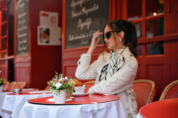 Trendy lady touches her glasses while seated at red terrace table