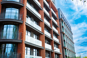 Obraz premium A modern brick building with large windows, balconies and glass railings, designed in a minimalist style, under a bright blue sky.