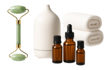Jade roller, aroma diffuser, essential oil bottles, and folded towels arranged elegantly on transparent background.