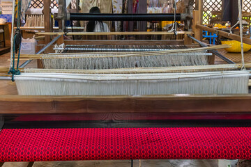 Silk weaving loom with vibrant red silk fabric in traditional silk factory in Chiang Mai in Chiang Mai, Thailand. Handmade craftsmanship, artistry of textile production, sustainable manufacture.