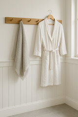 Minimal farmhouse bathroom wall close up white paneling plain white wall wooden peg rail hanging towel robe soft grey tile natural light