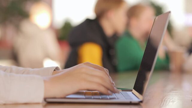 Woman is typing on a laptop. The laptop is open and the screen is black. The woman is wearing a white shirt