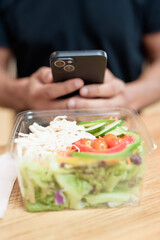Hand holding smartphone over healthy salad in mall food court, indoor lifestyle detail
