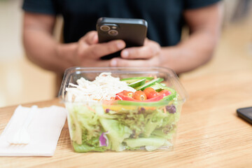 Hand holding smartphone over healthy salad in mall food court, indoor lifestyle detail