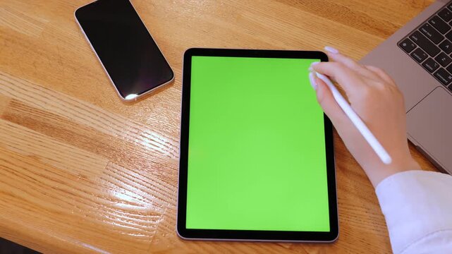 Woman is using a tablet with a green screen. She is touching the screen with a pen