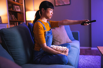 Serious woman watching TV at home late at night changing channels using remote control