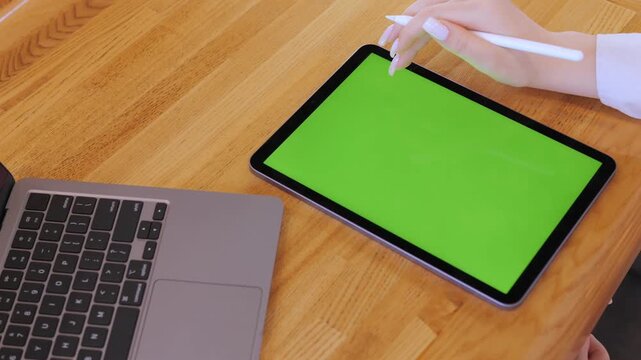 Woman is using a tablet with a green screen. She is touching the screen with a pen