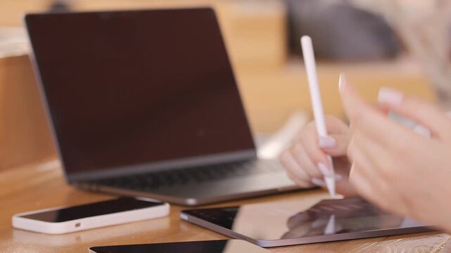 Person is writing on a tablet with a pen. The tablet is on a wooden table