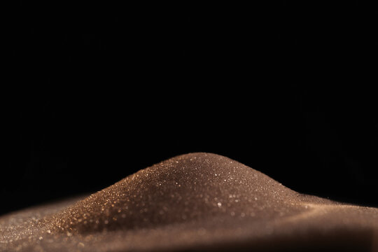 Gold sparkly hourglass sand on black background. Minimalist low key poto for concepts of time, travel to the desert