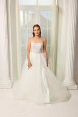 Fototapeta premium Bridal model posing elegantly in a white gown with soft lighting in a bright, classy room during a fashion showcase