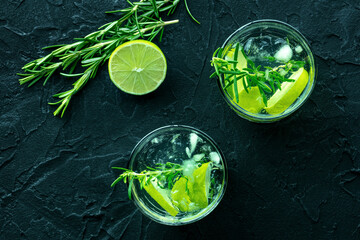 Gin tonic, overhead flat lay shot with rosemary and lime. Fresh summer cocktail with ice, on a black background