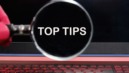 Business and Top tips concept, copy space. Top tips symbol. Concept words Top tips text appeared through a magnifying glass on a dim laptop screen