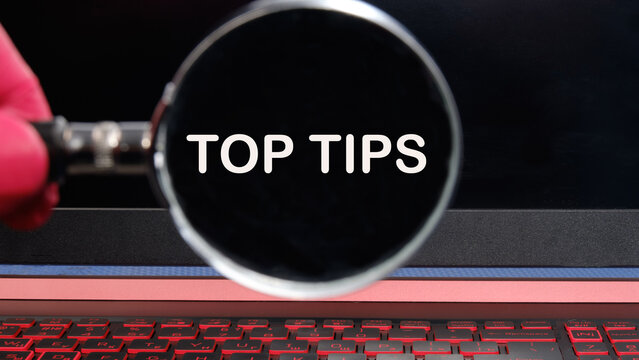 Business and Top tips concept, copy space. Top tips symbol. Concept words Top tips text appeared through a magnifying glass on a dim laptop screen