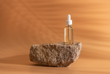 Dropper bottle with cosmetic product on rock podium on yellow background with shadows from palm leaves. Clean bottle with pipette and white cap, serum, essential oil