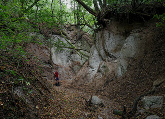 A hiker stands in the narrow Kőporos Gorge, surrounded by eroded rhyolitic tuff walls and clinging tree roots. The canyon is located in the Bükk region of northern Hungary. Editorial use only.