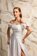 Elegant model poses in white dress with floral details against textured backdrop in a modern studio setting