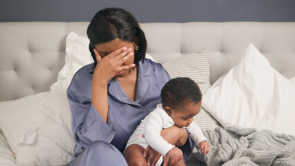 Postpartum Depression, Stressed Mother Sitting on Bed with Her Baby, Reflecting in an Emotional...