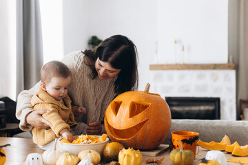 Family carving halloween pumpkin. Happy mother and cute baby son cutting pumpkin on table with...