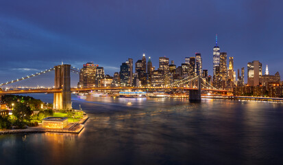 Naklejka premium Elevated view of New York City skyline at dusk with Brooklyn Bridge, Lower Manhattan skyscrapers and East River. Illuminated landmarks and buildings seen from DUMBO at twilight