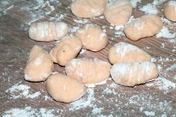 Fototapeta premium Close up of gnocchi pasta beinng made raw on wooden background covered in flour