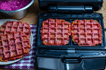 Modern open waffle iron with teflon coating with cooked zucchini, beetroot and herb waffles on wooden table, closeup, top view. Electric waffle maker in the home kitchen