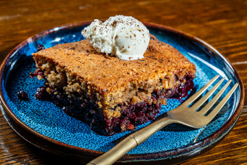 Plate with piece of fresh baked blueberry cobbler and ice cream on wooden background, closeup. Homemade berry cobbler ready to eat