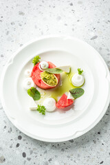 Artfully plated gourmet appetizer with watermelon, avocado, cream, and herbs on a white dish. Vibrant colors and elegant styling ideal for culinary themes.