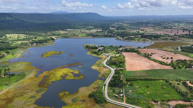 Drone footage of aerial view of Lam Phra Phloeng reservoir and surrounding farmland in Wang Nam Khiao, Nakhon ratchasima, Thailand. Scenic landscape of countryside with curved rural roads 