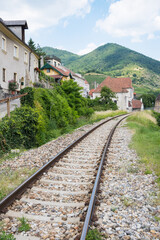 Abandoned train tracks splitting through forgotten village in front of a cloudy hill