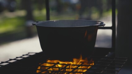 Cooking pot stands on a grate with a large flame of fire, cooking outdoors in a saucepan, outdoor...