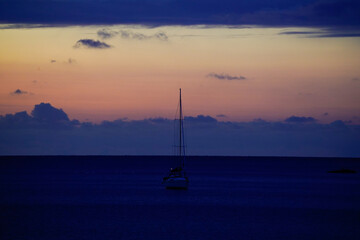 A quiet sailboat, silhouetted against the pale, purple-blue morning sky and the calm, dark sea. Sun and clouds at dawn on the Baltic Sea beach of 18586 G&ouml;hren, R&uuml;gen Island