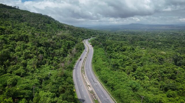 Drone footage of the aerial view of a winding road cutting through lush green forest. Scenic highway number 304 in Thailand links the Bangkok area to Nakhon Ratchasima in the northeastern region