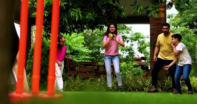 Indian family playing cricket bowling in home garden, spending quality fun time together with kids parents enjoying outdoor activity, cheerful Asian siblings and adults bonding during backyard match