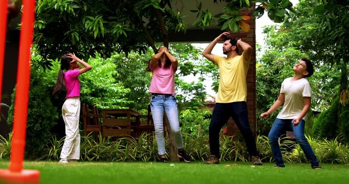 Indian family playing cricket bowling in home garden, spending quality fun time together with kids parents enjoying outdoor activity, cheerful Asian siblings and adults bonding during backyard match